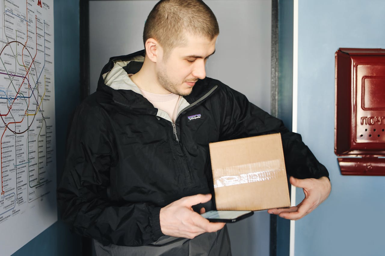 Man in Black Zip Up Jacket Holding Brown Cardboard Box